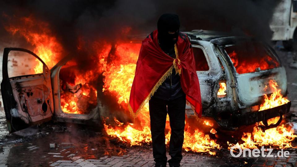 Ein Demonstrant, der sich in eine albanische Flagge gehüllt hat, steht während einer regierungskritischen Demonstration in Tirana vor dem Büro des Ministerpräsidenten vor einem brennenden Auto. Bild: Hameraldi Agolli/AP/dpa
