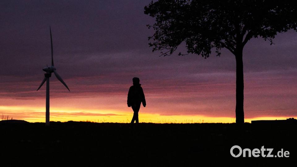 Eine Frau spaziert vor der vom Sonnenaufgang verfärbten morgendlichen Wolkenkulisse bei Hannover. Bild: Julian Stratenschulte/dpa