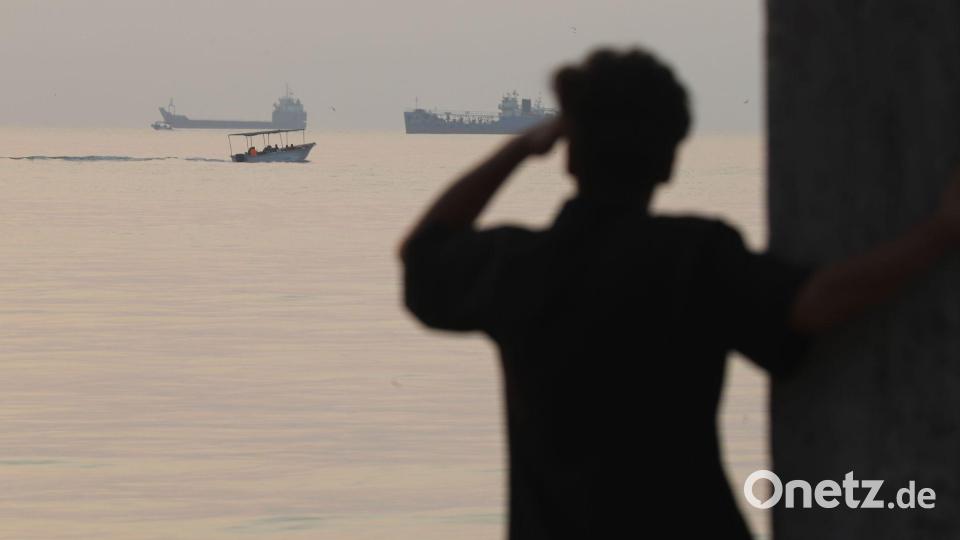 Ein Mann blickt aufs Wasser, während ein kleines Boot an Frachtschiffen vorbeifährt, die in der Straße von Hormus vor Bandar Abbas im Iran vor Anker liegen. Bild: Amirhosein Khorgooi/ISNA/AP/dpa