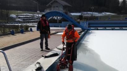 Einer sichert, der andere sägt die Eisschicht auf. Obwohl die Sonne scheint, bibbern Horst Lindner (links) und Benjamin Höllerer (rechts) bei minus 11 Grad Celsius im Freibad. Der Druck, der durch das Eis entsteht, kann die Fliesen im Freibad zum Bersten bringen. 	Bild: exb