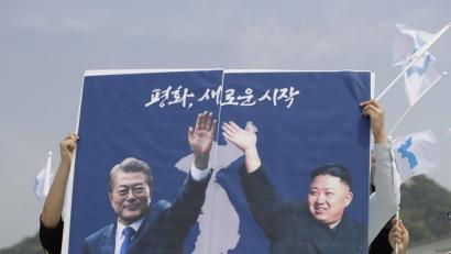 Südkoreaner halten ein Plakat, das Moon Jae In (links), Präsident von Südkorea, und Kim Jong Un, den Machthaber in Nordkorea, zeigt. 
 	Bild: Lee Jin-Man/dpa