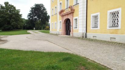 Bild: e
Die schadhafte Sauerzapfstraße führt direkt am Schlosseingang vorbei. Auf dem Grünstreifen neben der Straße soll ein Gehweg für Fußgänger errichtet werden.