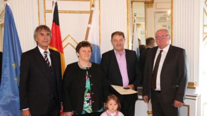 Bild: exb
Regierungspäsident Axel Bartelt (links) und der Oberviechtacher Bürgermeister Heinz Weigl (rechts)  bedanken sich bei Christa und Martin Biegerl (Mitte) mit Enkelin Franziska für ihren jahrelangen Einsatz.