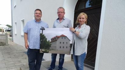 Bild: hou
Zeit für ein Geschenk, das der Bürgermeister aus eigener Tasche
finanzierte: Christian Ziegler (links) üerreichte ein großformatiges Bild vom renovierten Dorfwirtshaus an Investor Hans Gradl und dessen Ehefrau Nadja.
