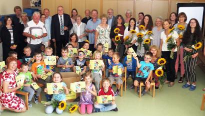 Bild: Dobmeier
Die schulvorbereitende Einrichtung mit Leiterin Ulrike Grajer (Sechste von rechts) feiert 25-jähriges Bestehen. Die Kinder halten den neuen Flyer. Sonnenblumen gibt es für langjährige Mitarbeiter.