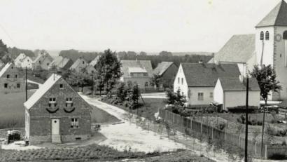 Bild: Archivbild
Fronleichnam 1954:. Die Straße ist mit Birken geschmückt und mit Schilf bedeckt. Rechts ist der spätere Schulgarten zu sehen. Einige Parzellen sind noch unbebaut. Die Kirche wurde im August 1951 eingeweiht.
