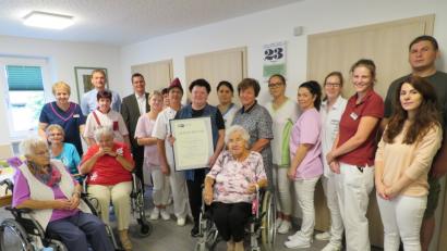 Bild: adj
Im Kreise der Bewohner und ihrer Kollegen wird sie ausgezeichnet: Hildegard Krischkowsky bekommt von Florian Rieder, Bürgermeister Ernst Schicketanz (hinten, von rechts) und Irina Löffler-Ilinov (Siebte von rechts) die Urkunde.