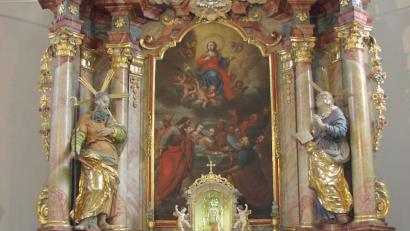 Bild: mma
Der Hochaltar der Frohnbergkirche zeigt die Krönung Mariens im Himmel. Der Thomas-Legende folgend sind darunter die staunenden Apostel vor dem leeren Grab der Gottesmutter abgebildet. In der Mitte befindet sich der Glasschrein mit dem Gnadenbild.