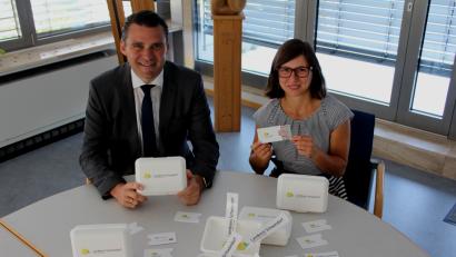Bild: Landratsamt Schwandorf
Landrat Thomas Ebeling und Regionalmanagerin Verena Frauenknecht präsentieren die mit dem neuen Logo bedruckten Brotzeitdosen und Führerscheinhüllen, die neben anderen Verwendungen für einen großen Bekanntheitsgrad des Logos sorgen sollen.