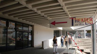 Bild: Hanna Gibbs
Namenswirrwarr: Über dem Eingang zum Theatersaal an der Universität prangt die Aufschrift „Studententheater“. Daneben wurden Plakate angebracht, auf denen „Theater an der Uni“ steht. Die Theatergruppe „ueTheater“ lädt stets ins „Elly Maldaque Theater“ ein.