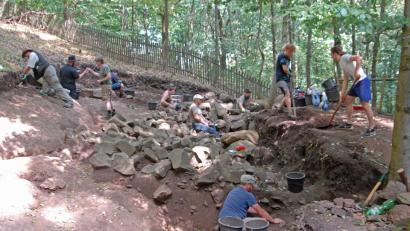 Bild: ow
Der untere Ringwall, die erste Verteidigungsbefestigung am Fuße der Geröllhalde, ist auch heuer wieder ein Schwerpunkt der Ausgrabungen. Dr. Hans Losert (Dritter von links) berichtete, dass in diesem Bereich zwischen den angehäuften Vulkansteinen bereits besonders viele Fundstücke entdeckt wurden.