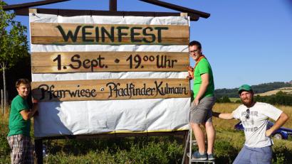 Bild: bkr
Manuel Schraml, David Maschauer und Jonnathan Scharf führen das Organisationsteam an. Sie weisen mit einer Tafel am Ortseingang auf das Weinfest hin.