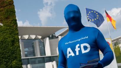 Bild: Paul Zinken/dpa
Alternative Montur: Ein komplett verhüllter Unterstützer der AfD mit der Aufschrift „Verfassungsheld AfD“ auf der Brust seines Ganzkörperanzugs verteilt beim Tag der offenen Tür der Bundesregierung vor dem Kanzleramt Informationsbroschüren der Partei.