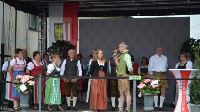 Bild: gi
Bürgermeister Hermann Ach stellt bei einem von Martina Kohlmann geführten Interview den Genussort Moosbach vor. Im Hintergrund die OWV-Volkstanzgruppe.