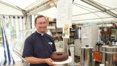 Bild: swo
Mächtig stolz zeigt sich Pfarrvikar Christian Preitschaft bei der Abgabe von Nummer zehn seiner zwölf Bananen-Schokoladenkuchen am Kuchenstand der Pfarrei.