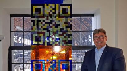 Bild: pz
Rainer Schmitt neben einem Glaskunstwerk, das schon vor einigen Jahren bei einer Baumesse präsentiert wurde. Es zeigt die QR-Codes der Glashütte Lamberts und von Schmitts Derix Glasstudios. Es verarbeitet das in handwerklicher Tradition gefertigte Produkt seit vielen Jahren.