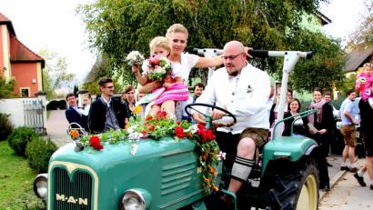 Bild: ds
Auf dem festlich geschmückten Traktor macht sich das frisch vermählte Brautpaar mit Töchterchen Antonia auf den Weg zum Kirchenreinbacher Gasthaus Goldene Krone, wo die Hochzeitsfeier ihre Fortsetzung nimmt.