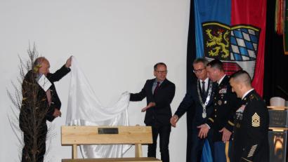 Bild: stg
Der ehemalige Leiter der VG-Geschäftsstelle, Robert Schön, und Partnerschaftsbeauftragter Martin Graser enthüllen eine Sitzbank, die an das Jubiläum erinnern soll. Sie ist ein Geschenk von Bürgermeister Werner, das unter anderem für Lieutenant Colonel John W. Copeland und Command Sergeant Major Joshua Kreitzer (von links) vom 709th Military Police Battalion bestimmt ist.