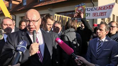 Bild: Wera Engelhardt/dpa
Peter Altmaier (CDU), Bundesminister für Wirtschaft und Energie, gibt In Redwitz ein Interview. Im Hintergrund demonstrieren Menschen gegen neue Stromtrassen.