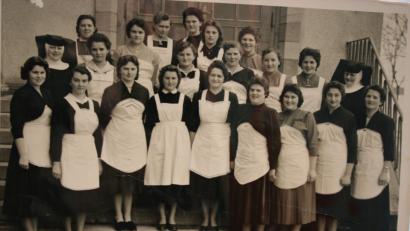 Bild: gpa
Erwartungsvoll und adrett in weißen Schürzen, ihrer „Dienstkleidung“, marschieren sie 1958 auf, die „Kocherln“, die Teilnehmerinnen an einem Koch- und Hauswirtschaftskurs im damaligen Elisabethenheim. Schwester Rodeberta (rechts) weiht sie in die Geheimnisse der Kochkunst ein, Schwester Edelhilde (links) gibt den jungen Damen Unterricht im Nähen.