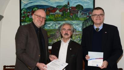 Bild: bey
Euregio-Egrensis Geschäftsführer Harald Ehm (links) und Stellvertreter Alexander Dietz (rechts) übergeben Bürgermeister Karl-Heinz Preißer den Zuwendungsbescheid über 5400 Euro aus Mitteln der Europäischen Union.