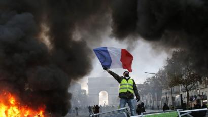 Bild: Michel Euler/AP/dpa
Ein Demonstrant mit einer gelben Weste schwenkt die französische Flagge neben einer brennenden Barrikade auf der Prachtstraße Champs Elysée mit dem Arc de Triomphe im Hintergrund. Die französische Polizei setzte Tränengas- und Wasserwerfer ein, um die gegen die Steuererhöhungen für Benzin und Diesel Demonstrierenden in Paris zu zerstreuen. Tausende Demonstranten hatten sich in der Hauptstadt versammelt und Straßenblockaden errichtet.
