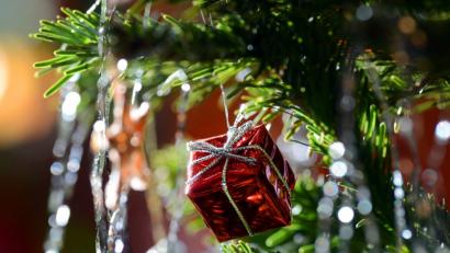 Bild: Jens Kalaene/dpa
Ein kleines rotes Geschenkpaket als Weihnachtsbaumanhänger und Lametta hängen an einem Weihnachtsbaum.