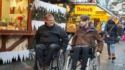 Bild: gld
Häufig sind die wirklich hilfreichen Dinge für Rollstuhlfahrer die, die unbewusst so gemacht werden. Die Höhe der Preisschilder in den Buden zum Beispiel. Alexander Grundler (links) erklärt mir, worauf es ankommt, damit alle voll an der Gesellschaft teilhaben können.