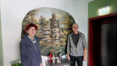 Bild: bsc
Im Flur der Pension grüßt ein Gemälde, das den Weißenstein im Steinwald zeigt, die ankommenden Gäste. Sabine (links) und Stefan Friebus wissen mittlerweile viel über das herrliche Wandergebiet und beraten ihre Gäste auch bei ihren Ausflügen.