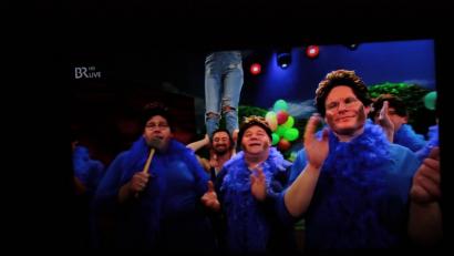 Screenshot: ui/Quelle: BR
Im blauen Kleid mit Federboa ehren die Künstler, darunter Peter Fuhrmann und Lucky Schieder (von rechts) von der Altneihauser Feierwehrkapell'n, beim Finale in Veitshöchheim die "Mutter des Frankenfaschings" Barbara Stamm. Anschließend feiern sie mit ihr bis zum Frühstück weiter.