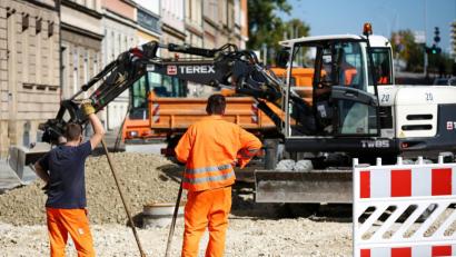 Bild: David Ebener/dpa
Zwei Bauarbeiter schauen ihrem Kollegen in einem Bagger beim Verteilen von Kies an einer Baustelle zu.