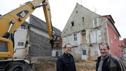 Bild: Wolfgang Steinbacher
Der Anbau ist abgerissen, an seiner Stelle entsteht ein Neubau, der das künftige Pfarrhaus (rotes Gebäude) barrierefrei machen wird. Von links: Pfarrer Thomas Helm, Architekt Georg Zunner.