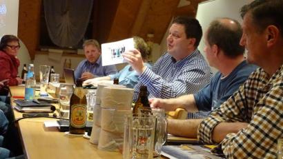 Bild: Houschka
Letzter Organisatorentreff vor dem großen Fest: Bürgermeister Christian Ziegler hat Bilder von Bands und Kapellen dabei, die am ersten Maiwochenende in Wolfring auftreten.