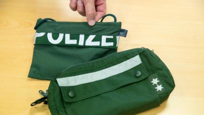 Bild: Daniel Karmann
Ein Brustbeutel und eine Fahrrad-Lenkertasche gefertigt aus Stoffen alter Polizei-Uniformen liegen auf einem Tisch.