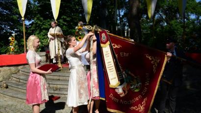 Bild: bey
Festbraut Julia Beugler heftet das von Stadtpfarrer Pater Hans Ring gesegnete Fahnenband an die Fahne der Pleysteiner Wehr an.