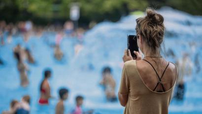 Bild: Jens Büttner/dpa
Eine junge Frau fotografiert im Schwimmbad mit ihrem Handy Kinder im Wasser.