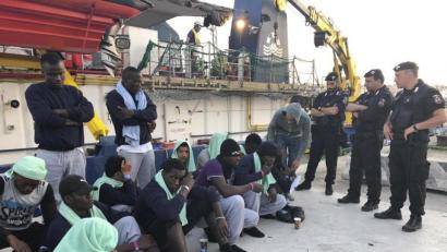 Bild: Annalisa Camilli/AP/dpa
Migranten vom Rettungsschiff "Sea-Watch 3" sitzen bewacht von Polizisten auf dem Steg im Hafen der Insel Lampedusa.