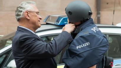 Bild: Daniel Karmann/dpa
Der bayerische Innenminister Joachim Herrmann (CSU) hilft einem Polizisten mit Kugelsicherer Weste einen neuen ballistischen Schutzhelm zu schließen.
