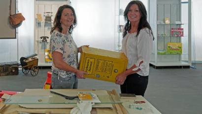 Bild: tr
Nicole Schuller und Marion Papsch (von links) tragen beim Aufbau der Ausstellung einen Briefmarkenautomat aus dem Jahr 1936.