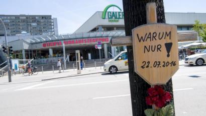 Bild:  Peter Kneffel/dpa
Ein Holzkreuz mit einem Schild und der Aufschrift "Warum nur! - 22.07.2016" hängt vor dem Eingang zum Olympia-Einkaufszentrum (OEZ).