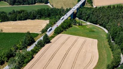 Bild: Armin Weigel/dpa
Autos fahren auf der Bundesstraße 16 zwischen Feldern und Wald (Luftaufnahme mit einer Drohne). Ein 46-Jähriger Jäger soll bei einer Gruppenjagd in dem Feld im August 2018 einen Schuss abgegeben haben, der einen Mann durch die Seitenscheibe eines vorbeifahrenden Autos an der Straße tödlich traf. Knapp ein Jahr nach einem mutmaßlichen Jagdunfall muss sich der Jäger vor dem Landgericht Amberg verantworten.