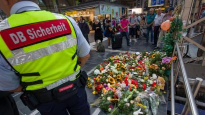 Bild:  Frank Rumpenhorst/dpa
Ein Mitarbeiter des Sicherheitsdienstes der Deutschen Bahn steht am Bahnsteig 7 im Frankfurter Hauptbahnhof vor den abgelegten Kerzen und Blumen. Ein achtjähriger Junge ist hier am Tag zuvor von einem Mann vor den einfahrenden ICE gestoßen und getötet worden.