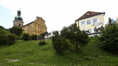 Bild: Petra Hartl
Der Neubau, der sich Richtung Kirche strecken wird, bleibt so flach und tief an den Hang geduckt – ohne diesen weiter als bisher abzugraben, wie der Bauherr versichert –, dass gar keine Chance bestehe, das Gotteshaus zu verdecken. Die alte Bergwirtschaft, die bis auf den neueren Anbau links äußerlich unverändert bleibt, tue das heute ja auch nicht.