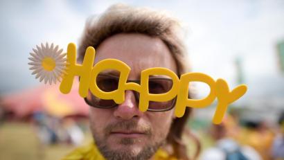 Bild: Ben Birchall
Ein Besucher eines Festivals in Großbritannien mit einer „Happy“-Brille. Foto: Ben Birchall/PA Wire