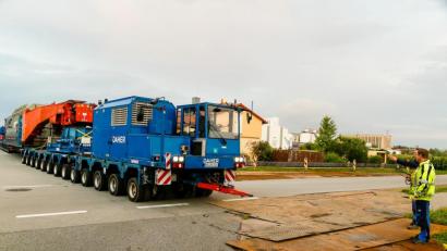 Bild: Hösamer
Gut 55 Meter und rund 546 Tonnen schwer lang ist der Schwerlastzug, der am Montagabend vom Müllkraftwerk durch die Alustraße (Bild) Richtung Umspannwerk Büchelkühn rollt. Transportiert wird ein 273 Tonnen schwerer Trafo, der in einem Tieflader mit Tragschnäbeln (rot) auf zwei jeweils 13-achsigen, je 700 PS starken Zugmaschinen ruht.