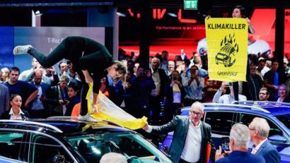Bild: Uwe Anspach/dpa
Während des Eröffnungsrundgangs von Bundeskanzlerin Merkel (CDU) auf der IAA versucht ein Mann am Stand von Volkswagen einer Aktivistin der Umweltschutzorganisation Greenpeace ihr Transparent mit der Aufschrift „Klimakiller“ zu entreißen.
