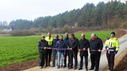 Bild: jp
Die beiden Bürgermeister Stefan Braun und Ludwig Lang (Mitte) durchschneiden symbolisch das Absperrband und nehmen die sanierte Gemeindeverbindungsstraße zwischen dem Hallerbrunnen (Hintergrund) und Pattershofen (Kastl) in Betrieb. Sie ist Teil des vielbefahrenen Fünf-Flüsse Radwegs.