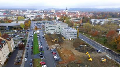 Luftbild: Michael Ascherl
Zwischen Leibnizstraße (links) und Dr.-Pfleger-Straße (rechts) heben Bagger die riesige Grube für das Quartier "Neue Naabwiesen" am Rand der Weidener Innenstadt aus. Auch die momentan noch von Oberpfalz-Medien genutzten Parkflächen in der linken Hälfte werden Teil der 9000 Quadratmeter großen Baustelle.