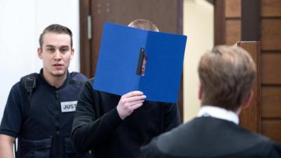 Archivbild: Federico Gambarini/dpa 
Der Angeklagte hält sich auf dem Weg in den Gerichtsaal einen Aktenordner vor das Gesicht. Dem 22-Jährigen wird der Mord an seiner Oma vorgeworfen. Er soll die 79-Jährige im Juli in Köln getötet haben, weil diese seinen Lebensstil kritisiert und ihn als „faulen Hund“ bezeichnet haben soll.