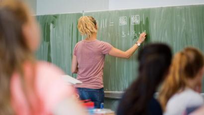 Symbolbild: Julian Stratenschulte/dpa
Eine junge Lehrerin schreibt an eine Schultafel.